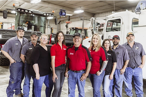 Group photo of the Regier Equipment team standing in the service shop surrounded by ag equipment.