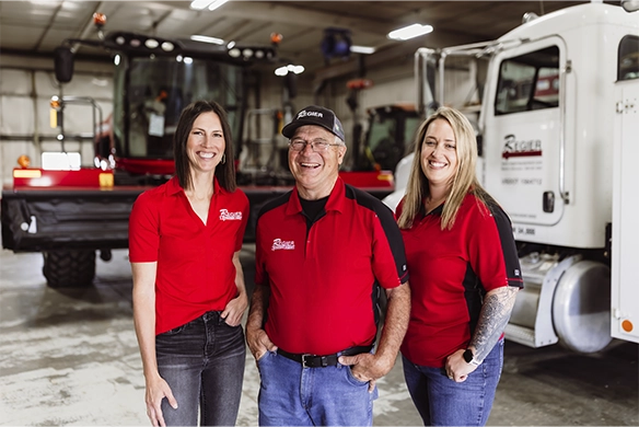 Three members of the Regier Equipment leadership team smiling together in the service shop.